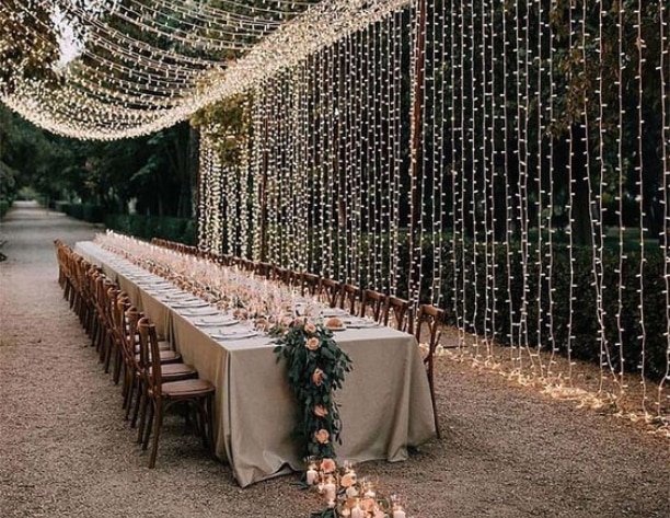 Event table set up outside with candles, florals and a string light drapery