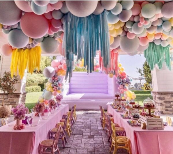 Party tables set with pink tablecloths and a balloon ceiling with bright colored balloons